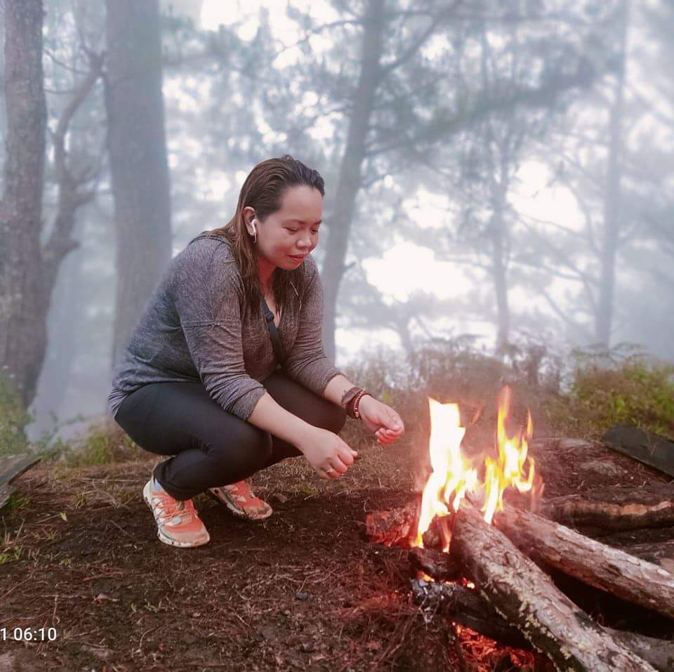 Woman squatting pensively by a campfire in foggy woods.